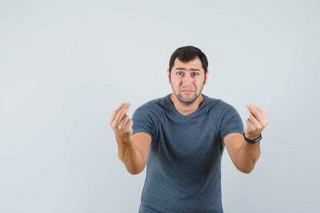 Young man doing money gesture in grey t-shirt and looking indigent 