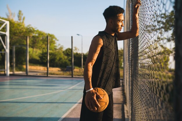 Young man doing sports, playing basketball on sunrise