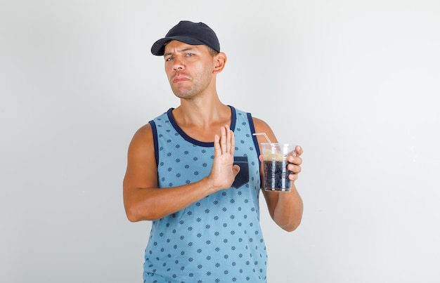 Young man doing stop sign to cold cola in blue singlet and cap