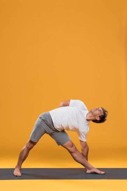 Бесплатное фото Молодой человек делает растяжку на коврик для йоги