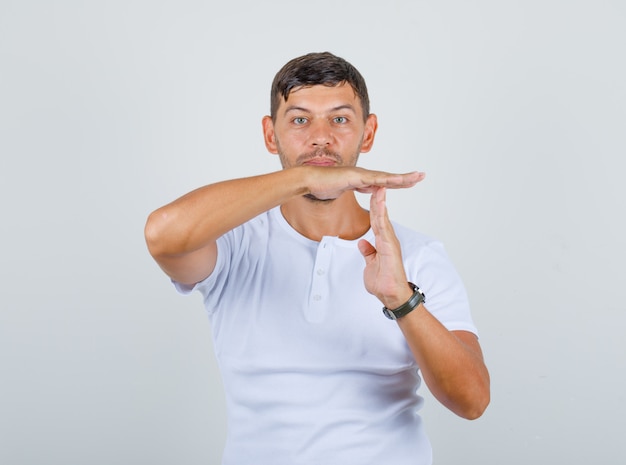 Young man doing time break gesture in white t-shirt, front view.