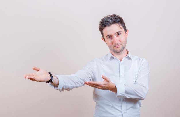 Free photo young man doing welcome gesture in white shirt and looking gentle