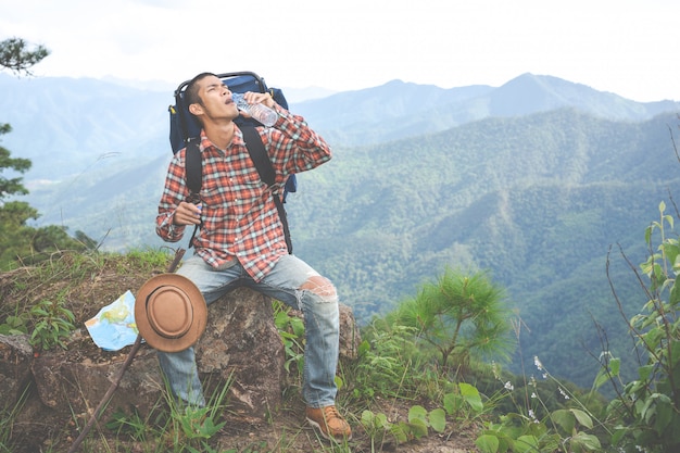 Young man drank water on a hilltop in a tropical forest along with backpacks in the jungle. Adventure, hiking