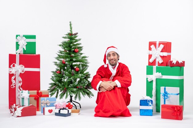 Young man dressed as Santa claus with gifts and decorated Christmas tree