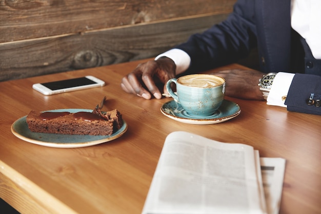 Young man dressed in formal suit having coffee and dessert in cafe