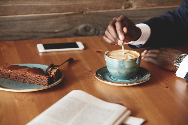 Young man dressed in formal suit having coffee and dessert in cafe