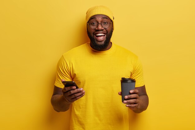 電話とコーヒーカップを保持している黄色の服を着た若い男