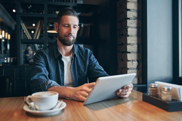 カフェでコーヒーを飲みタブレットコンピュータを使用している若者フリーランサー職場ランチ