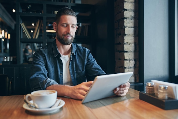 Young man drinking coffee in cafe and using tablet computer. Freelancer. Workplace. Lunch