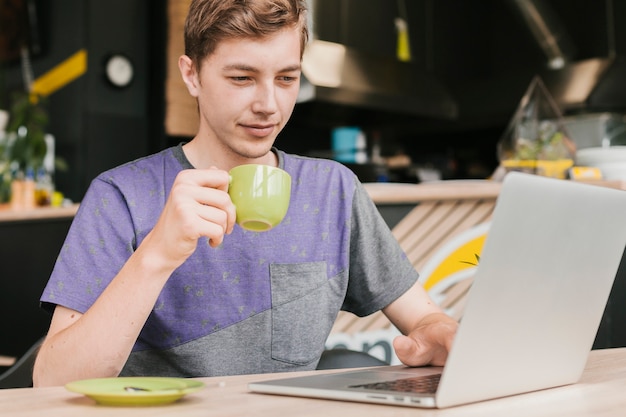 若い男がノートパソコンの前でコーヒーを飲む