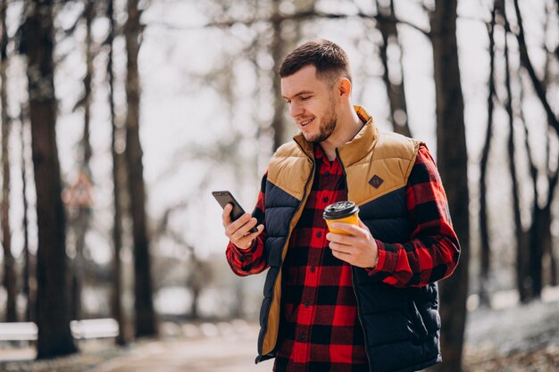 Young man drinking coffee in park and using phone