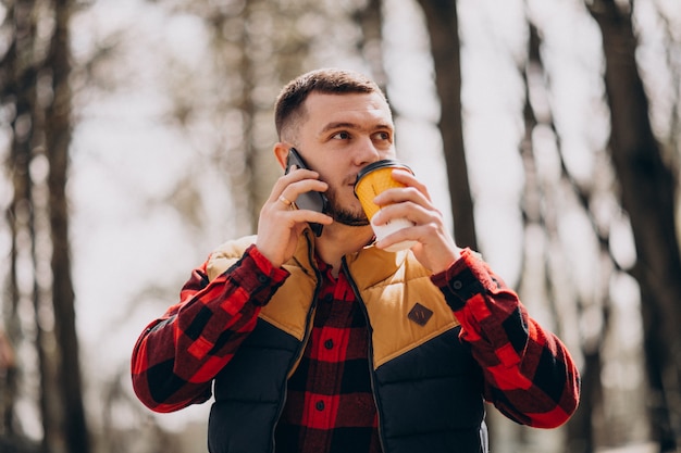 Caffè bevente del giovane in parco e nel telefono usando