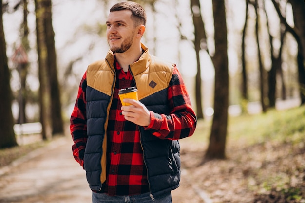 Young man drinking coffee in park and using phone