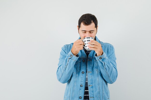 Giovane che beve caffè in t-shirt, giacca e sembra felice