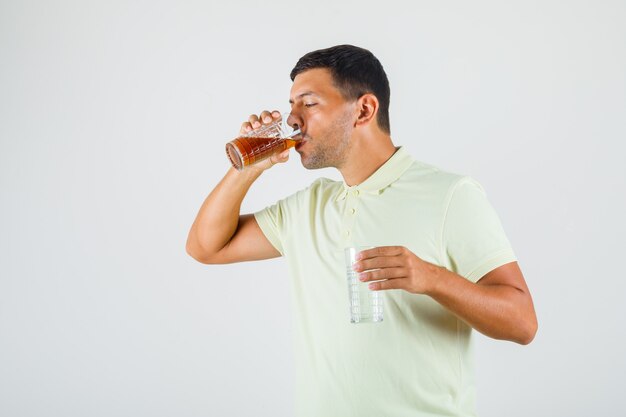 Tシャツに水のガラスを押しながらコーラを飲む若い男