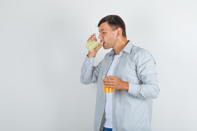 Young man drinking glass of juice in shirt