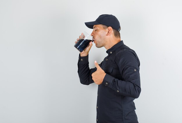 Young man drinking soda with thumb up in black shirt