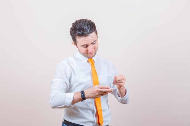 Young man drinking turkish coffee in white shirt, tie and looking careful