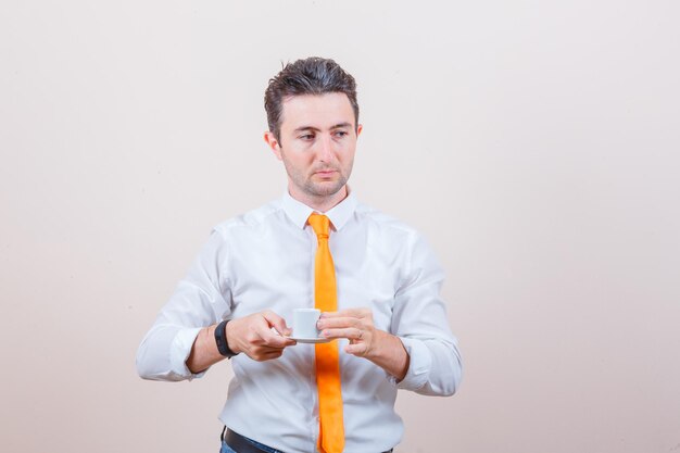 Young man drinking turkish coffee in white shirt, tie and looking thoughtful