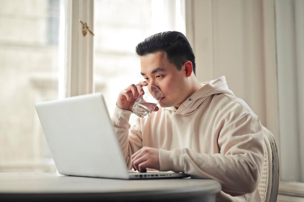 young man drinks a glass of water and works with computer