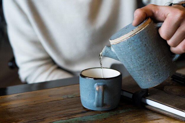 若い男はお茶を飲み、ラップトップで働き、フリーランサーはカフェで働いています