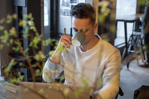 young man drinks tea and works on a laptop, freelancer working in a cafe