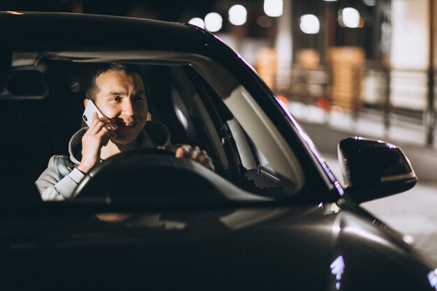 Young man driving his car at a night time and talking on the phone