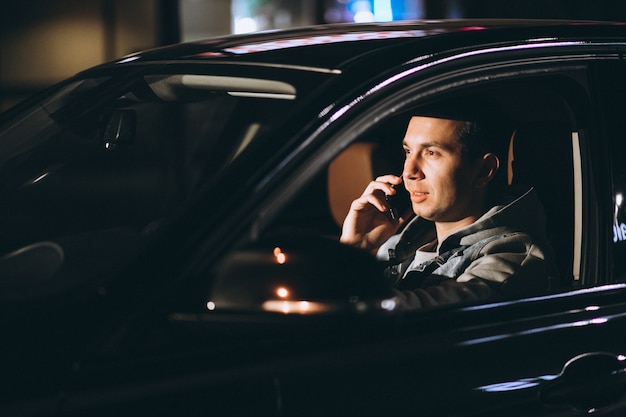 若い男が夜に彼の車を運転し、電話で話しています。