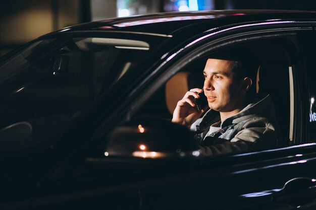 밤 시간에 그의 차를 운전하고 전화 통화하는 젊은 남자