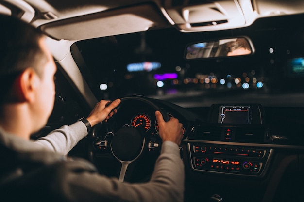 Молодой человек за рулем своего автомобиля в ночное время