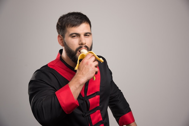 회색 벽에 바나나를 먹는 젊은 남자.