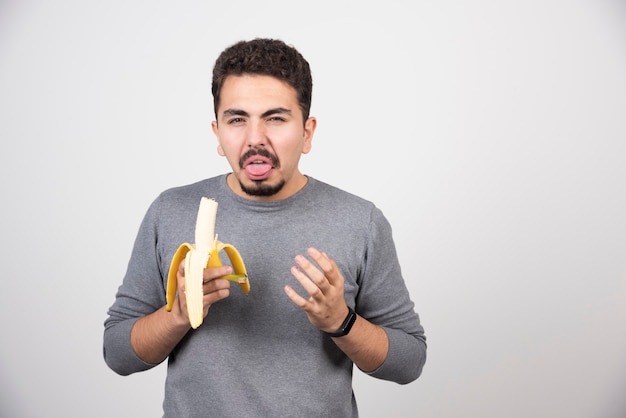 A young man eating a banana with disgust.