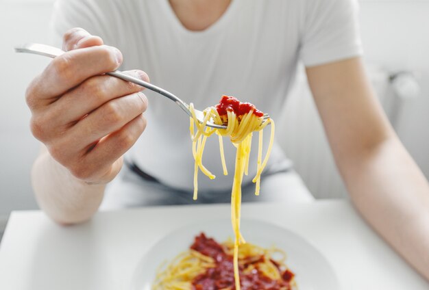 若い男がトマトソースのおいしいスパゲッティを食べます。閉じる。