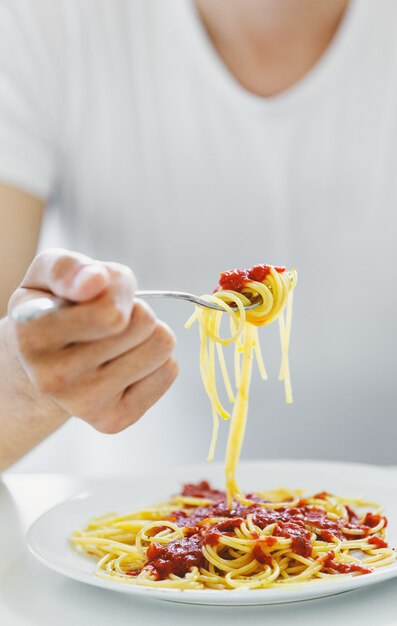 Young man eating tasty spaghetti with tomato sauce. Closeup.