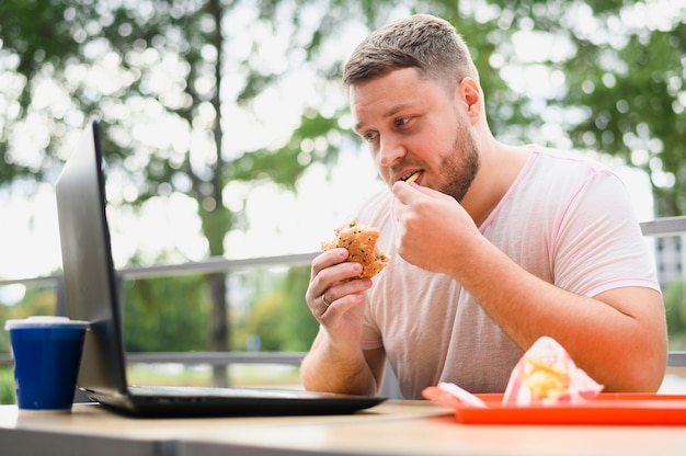 Free photo young man eating while looking at laptop