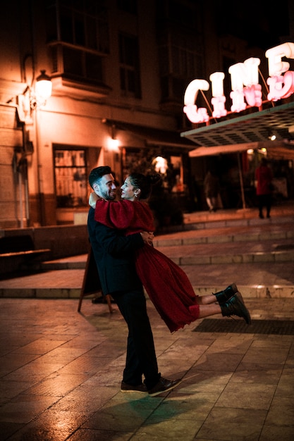 Young man embracing hanging laughing woman on street in evening