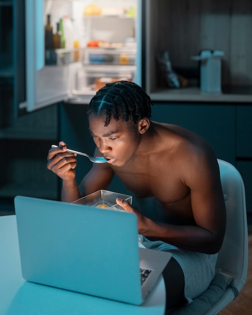 Бесплатное фото Молодой человек наслаждается закуской дома посреди ночи