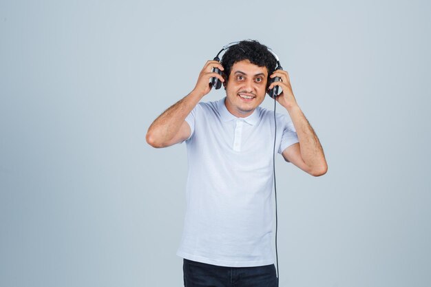 Young man enjoying music with headphones in white t-shirt and looking merry , front view.