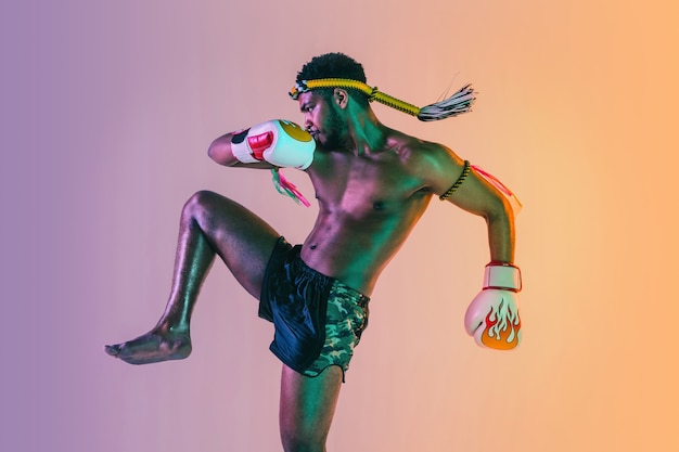 Young man exercising thai boxing on gradient background in neon light.