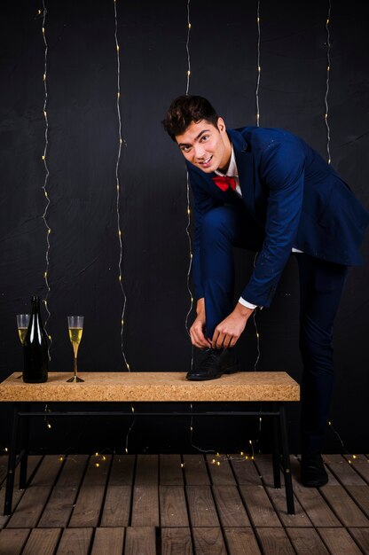 Молодой человек, закрепляющий обувь, кружит рядом с стеклом и бутылкой шампанского