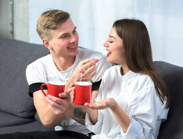 Young man feeding woman with marshmallow on couch 