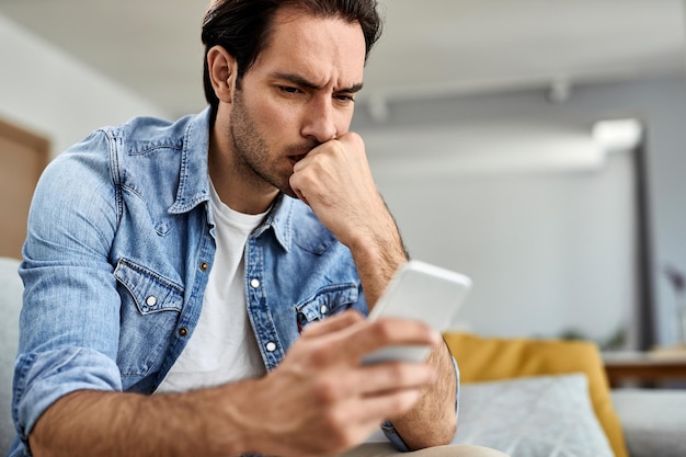 Free photo young man feeling worried while reading text message on mobile phone at home