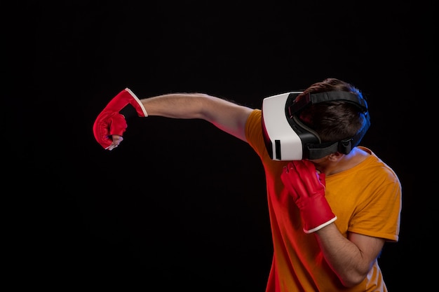 Young man fighting in virtual reality with mma gloves on black surface