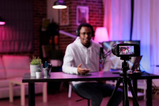 Young man filming podcast episode on camera in studio, live broadcasting online discussion to create social media content. Male influencer vlogging show with livestream equipment.