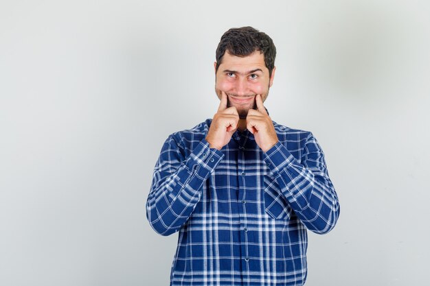 young man forcing cheerful smile in checked shirt and looking displeased