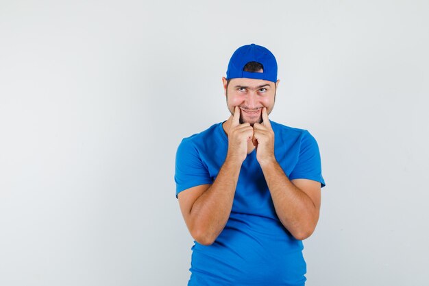 Молодой человек заставляет улыбнуться на лице в синей футболке и кепке