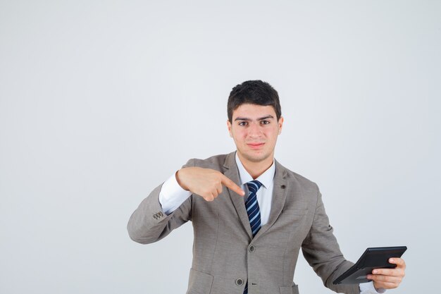 Young man in formal suit holding calculator, pointing to it