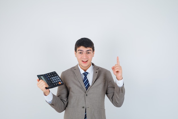 Young man in formal suit holding calculator, raising index finger