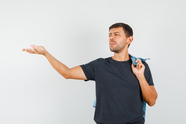 Young man gesturing in questioning manner holding jacket on back in t-shirt 