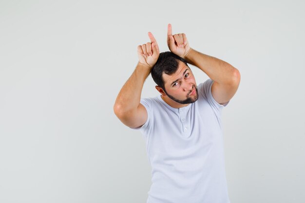 Young man gesturing with fingers over head as bull horns in t-shirt and looking funny. front view. space for text